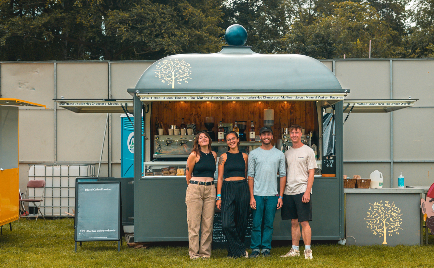 Four people standing in front of a food truck with a tree design on the side.